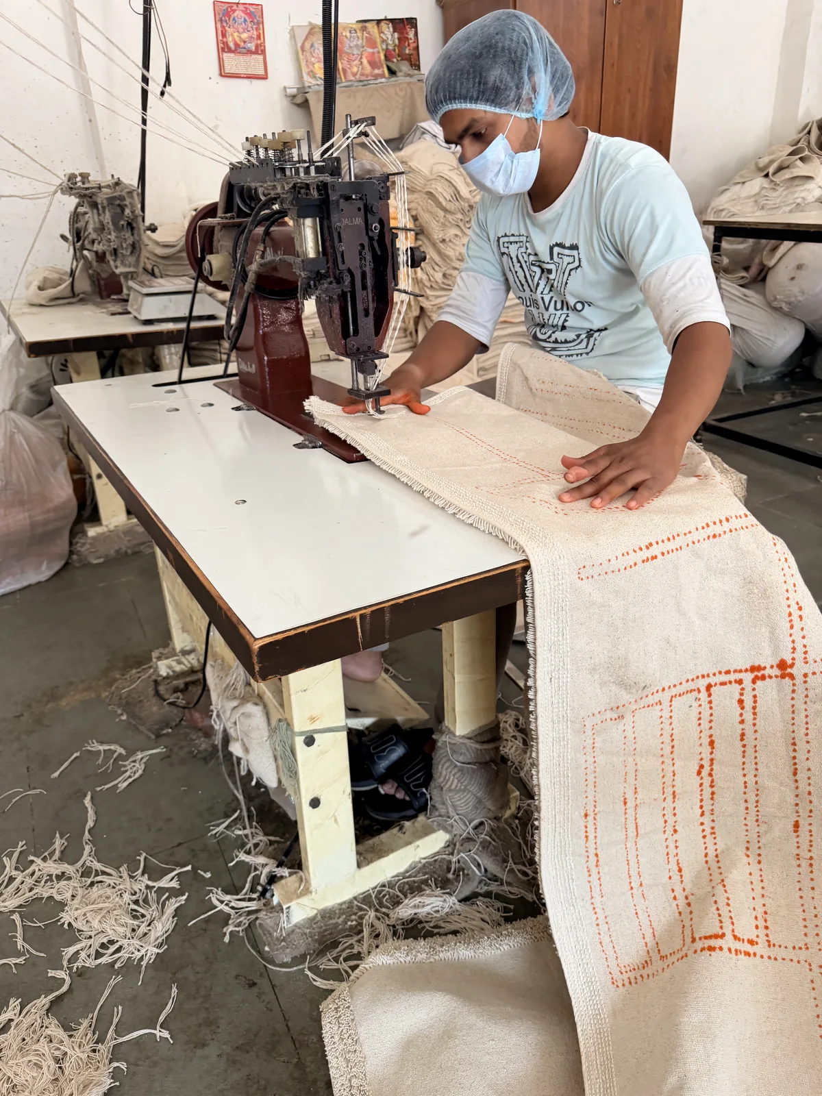 Design outlines marked in orange on the cotton backing of a rug being fed through a bench tufting machine