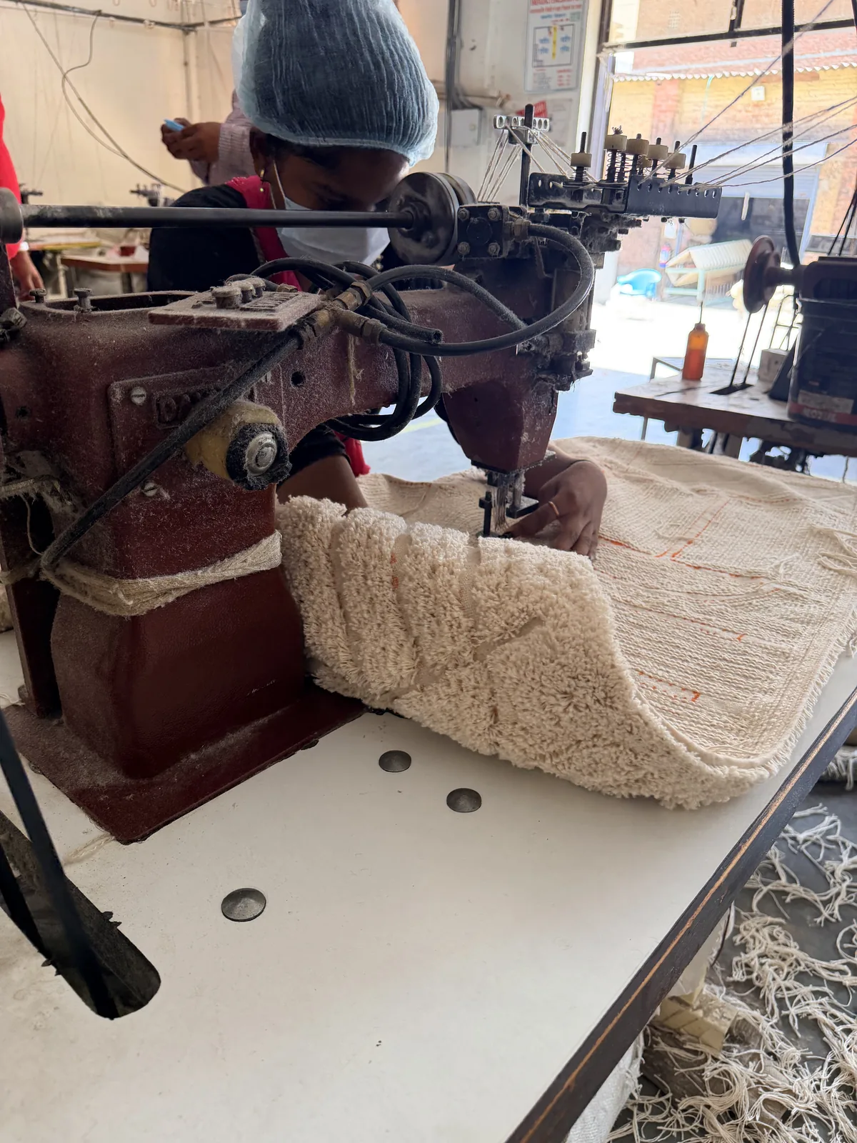 A tufter at a bench-mounted tufting machine working a cream rug, with completed carved pile visible on the finished section