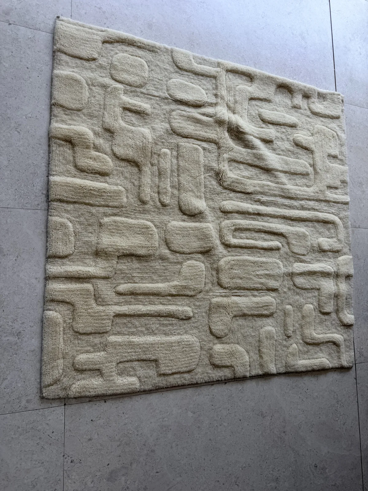 Full square carved bench-tufted rug with interlocking geometric relief shapes in undyed cream