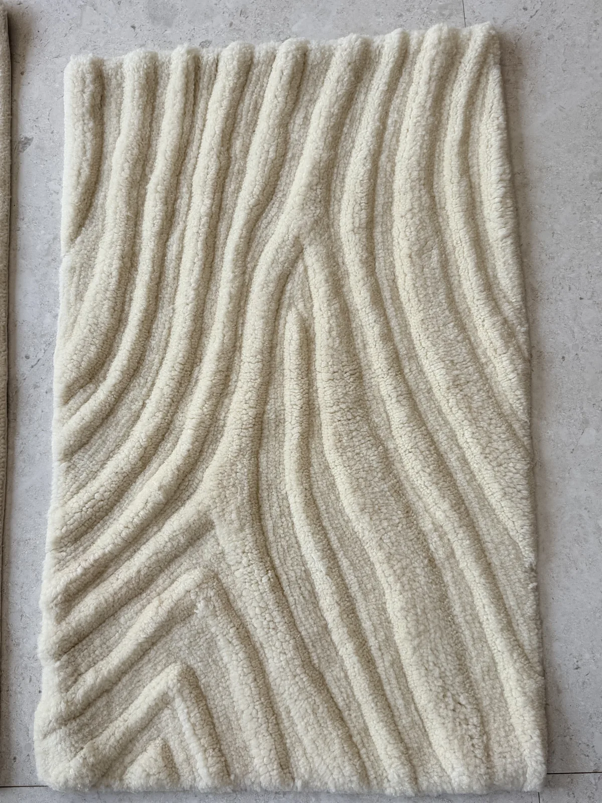 Full view of a carved bench-tufted rug with flowing wave relief in undyed cream wool