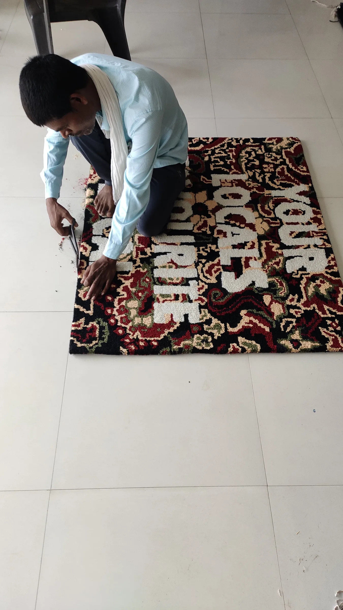 Loose pink and cream wool fibre covers the floor around a rug being carved