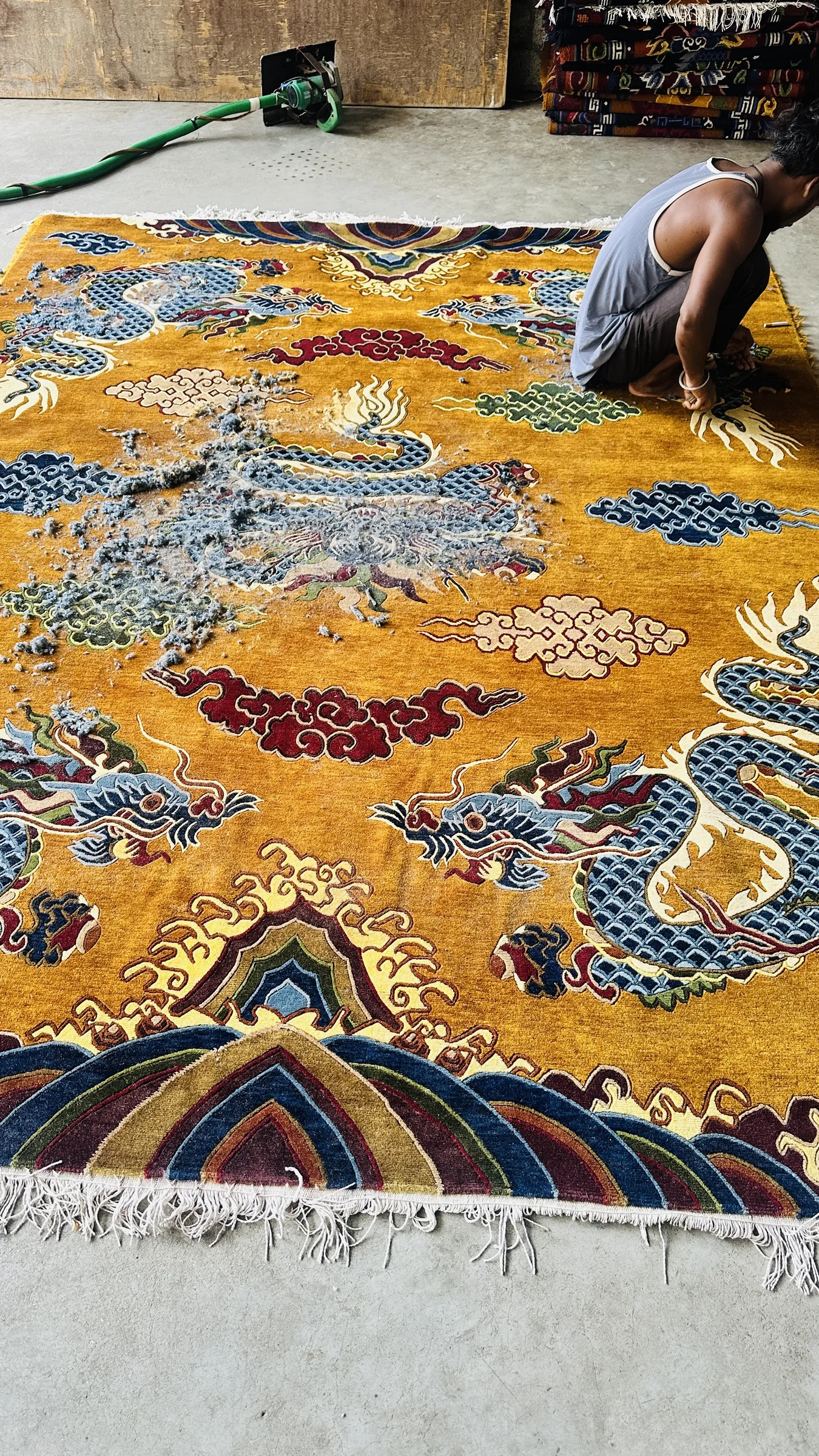 A hand-tufted yellow-gold traditional dragon-and-cloud rug being carved with hand shears