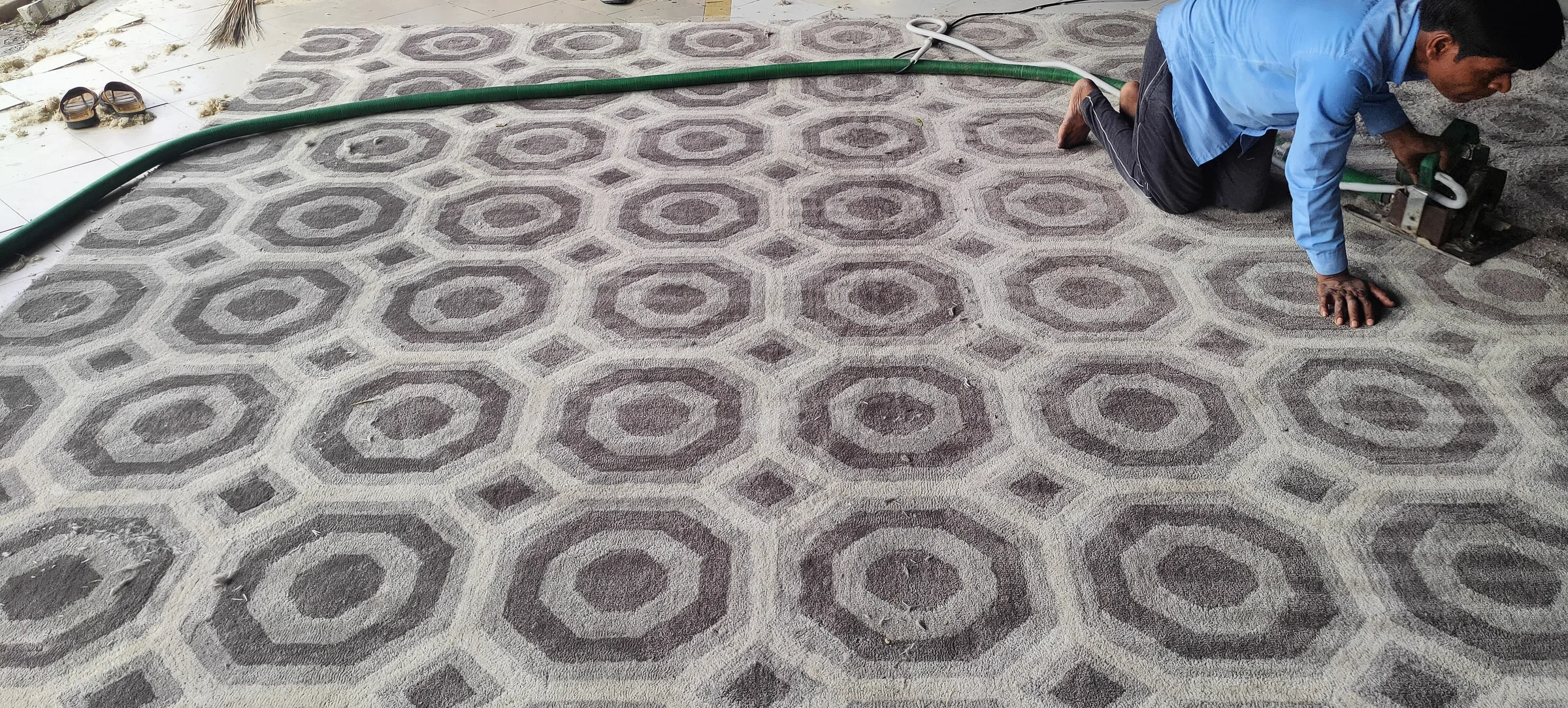 A finisher tracing the outline of a design with shears mid-carve on a tufted rug
