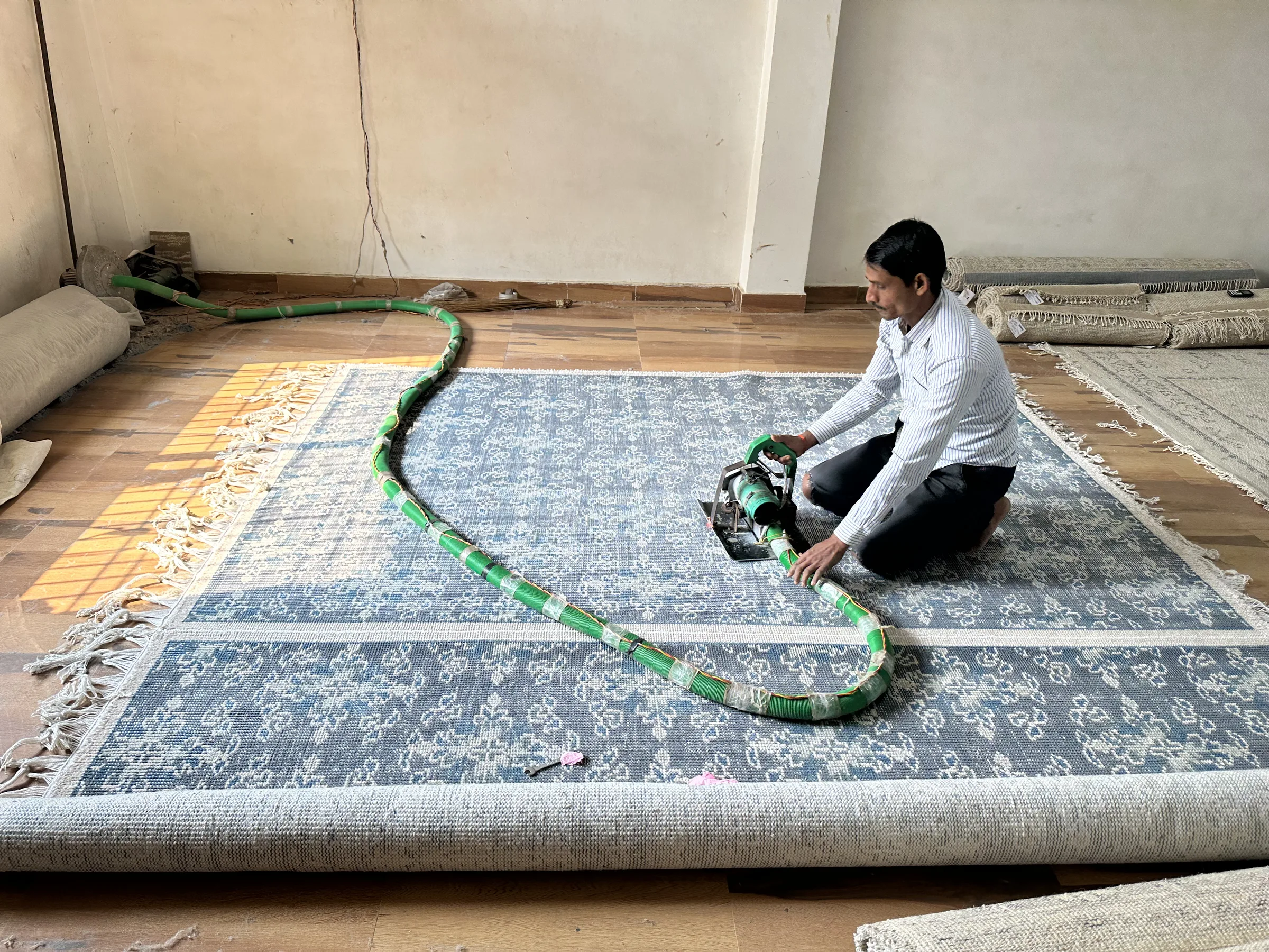 A finisher using a hand-held pile-lifter tool with green corrugated hose on a finished rug