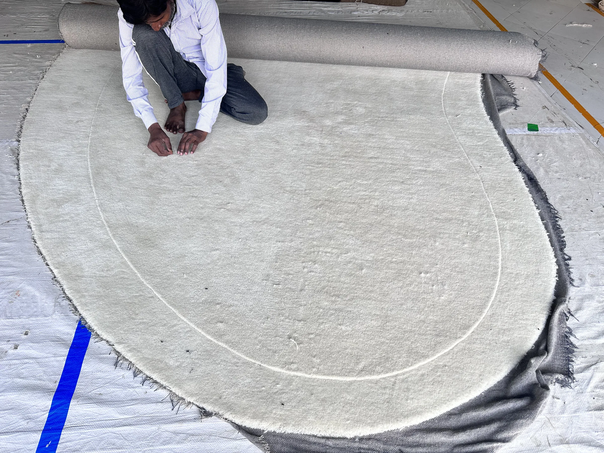 A finisher pressing the pile flat to inspect a cut line at the edge of an ivory round rug