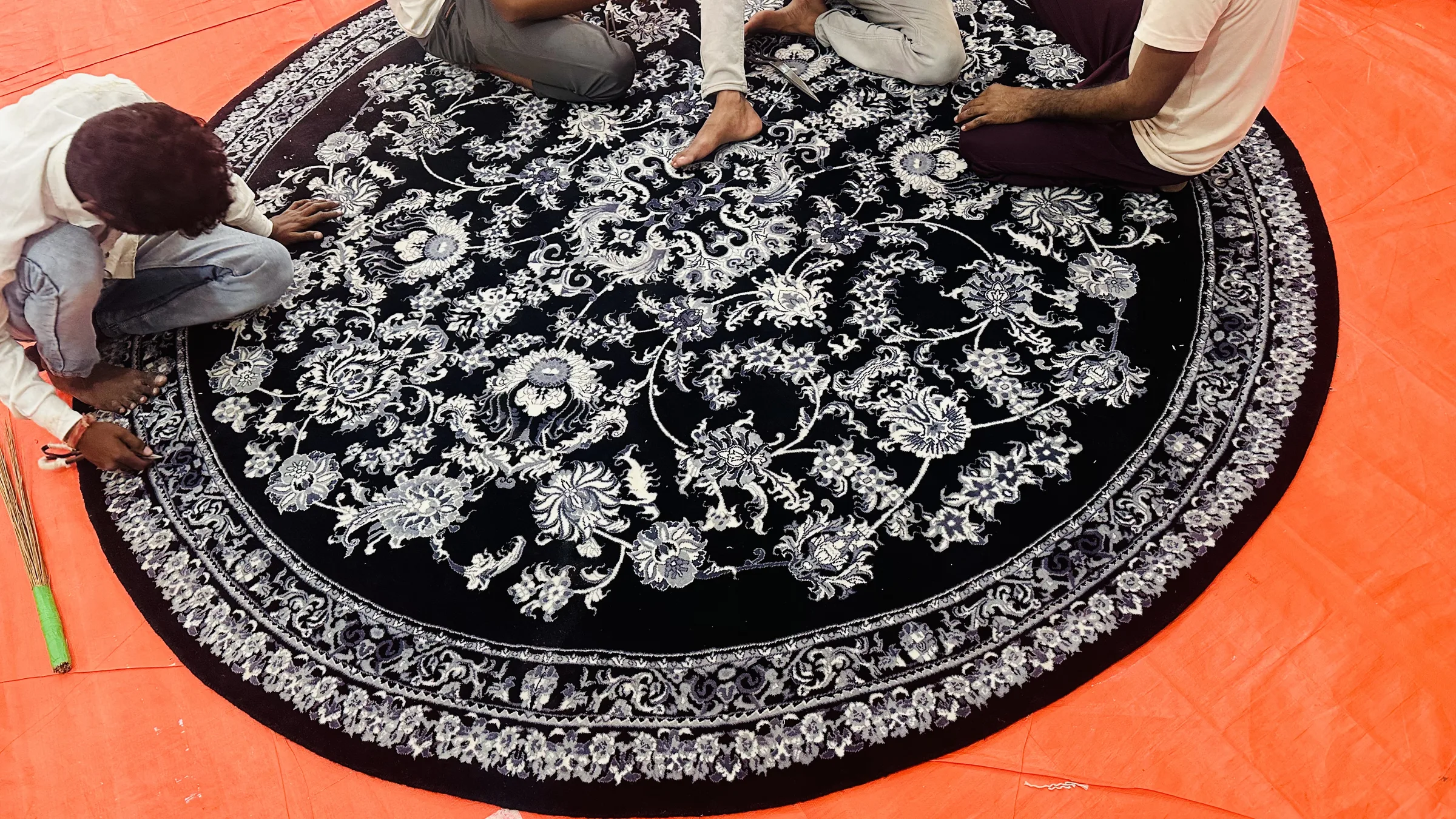 Two finishers carving a round black and white floral hand-tufted rug with long-blade shears