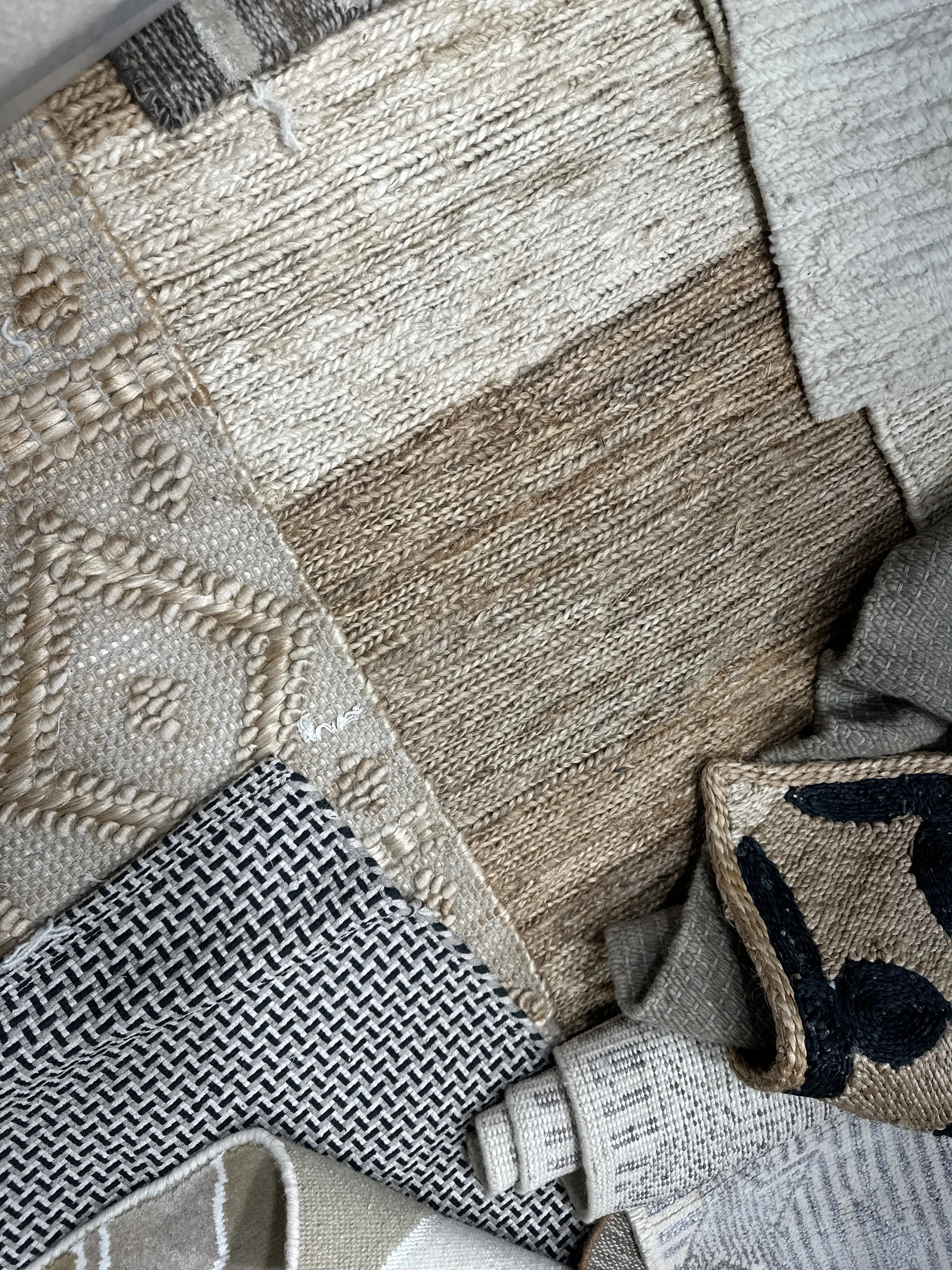 Overhead flatlay of neutral-toned rug samples in jute, cotton and wool with a range of weave textures