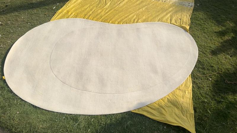 Kidney-shaped ivory rug with a bound curved edge, laid out to dry after finishing