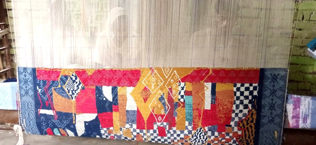 A contemporary flatweave rug on the loom in Bhadohi, in red, ochre and indigo