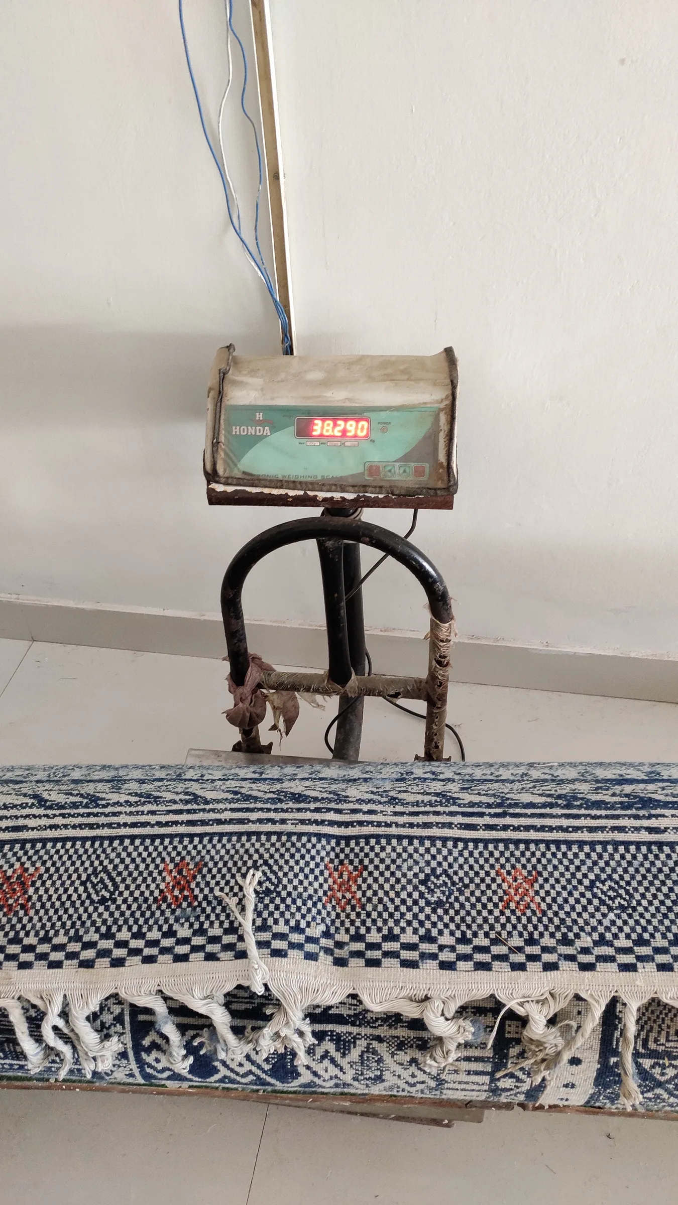 A blue and white kilim on the hanging scale, digital display reading 38290 grams