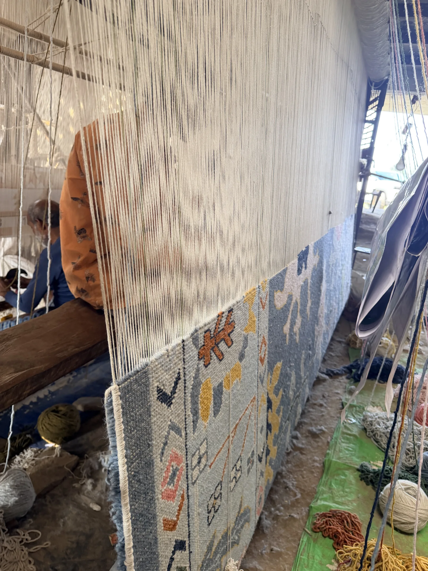 A hand-knotted rug in progress on the loom seen from the side, warp threads visible