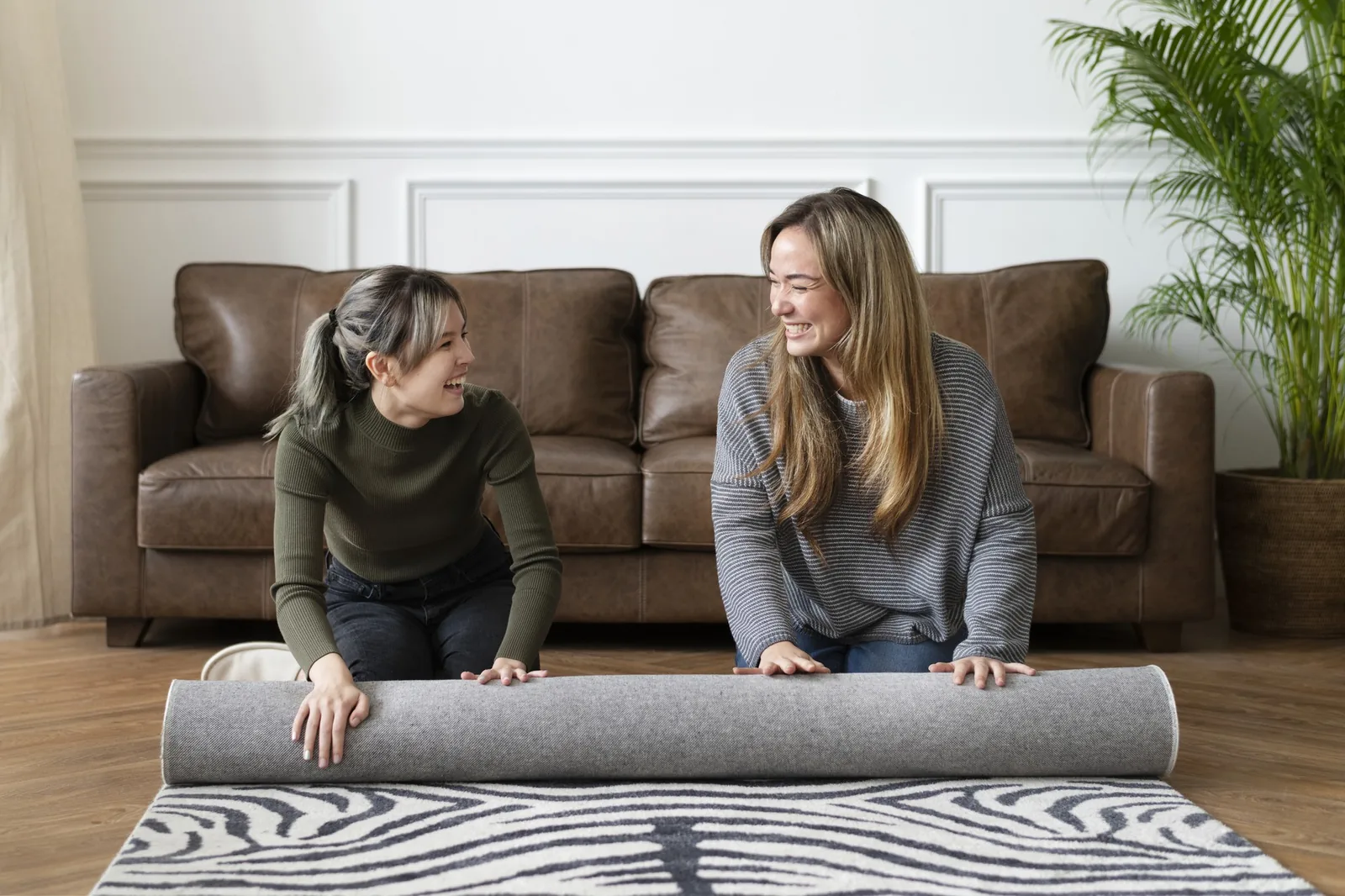 Two people laughing as they unroll a new handmade rug in a living room
