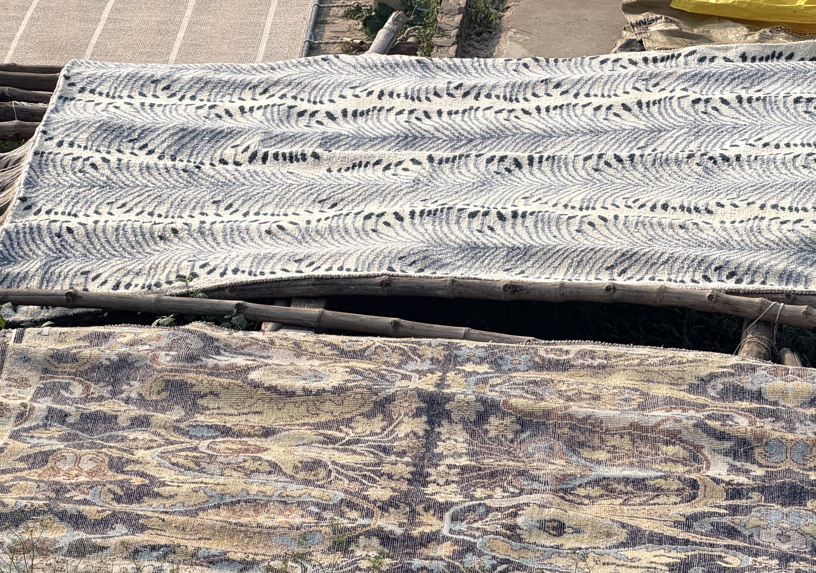 Stage 06 — a washed rug sun-drying flat on bamboo frames in the yard