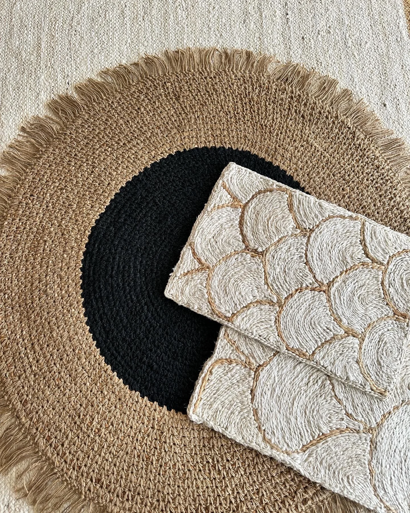 Overhead flatlay of a round jute rug beside a folded cream scallop-pattern jute-cotton rug