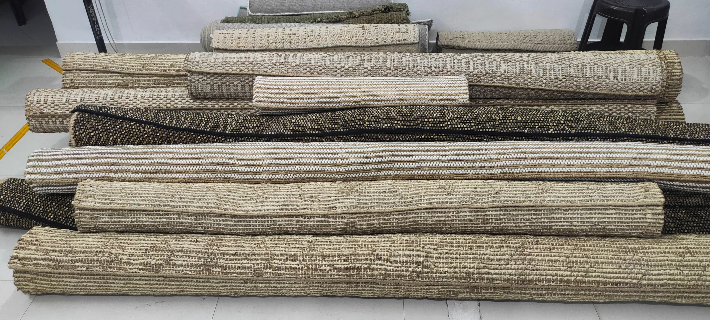 A stack of finished natural-tone jute and cotton flatweave rugs rolled and ready for the buyer