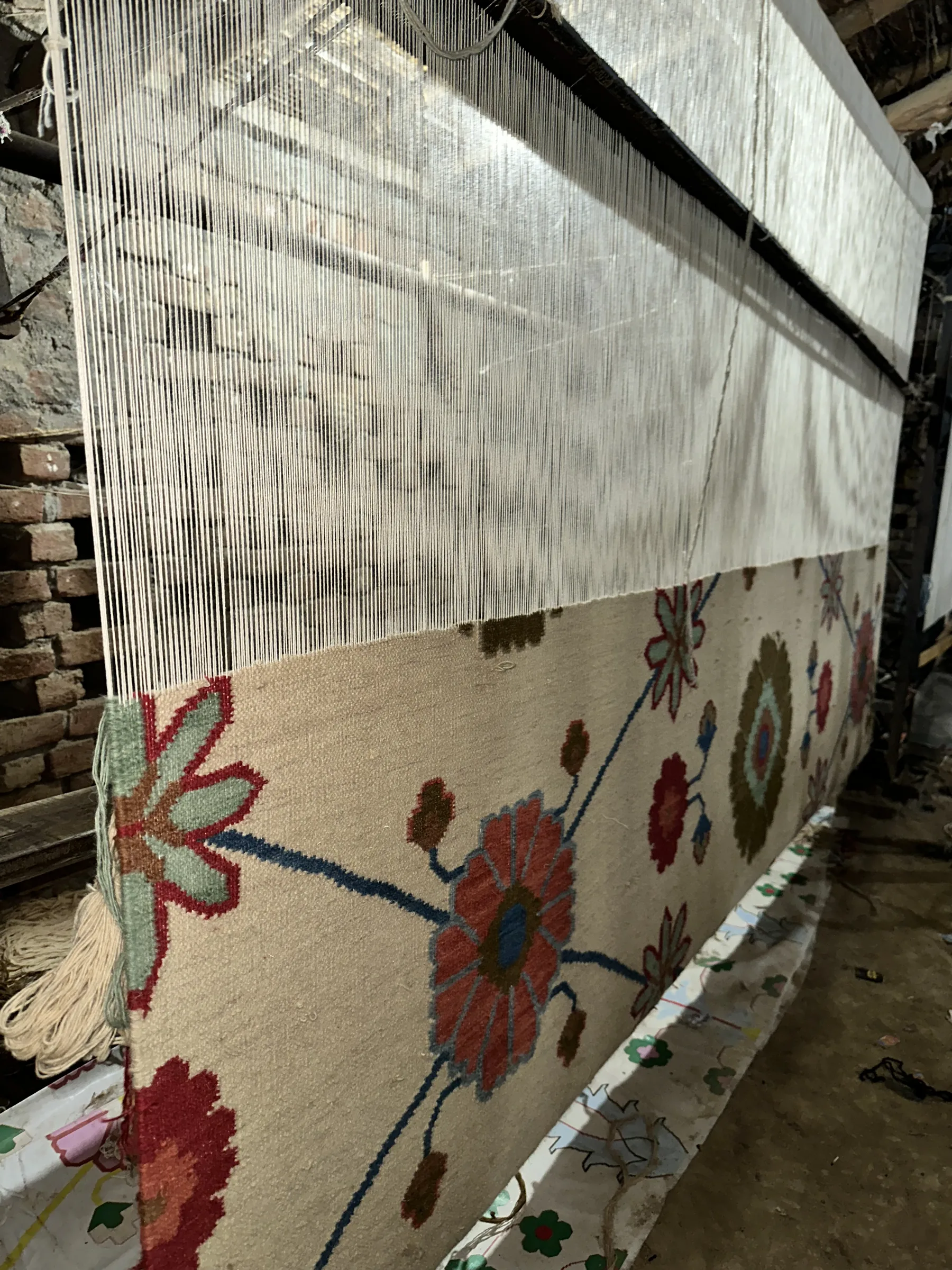 A traditional floral kilim being woven on a vertical loom with warp threads rising above
