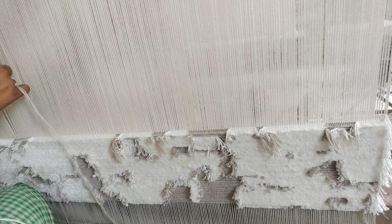 Rug on the loom &mdash; warp threads under tension above the weaving edge, with loop and cut pile emerging row by row
