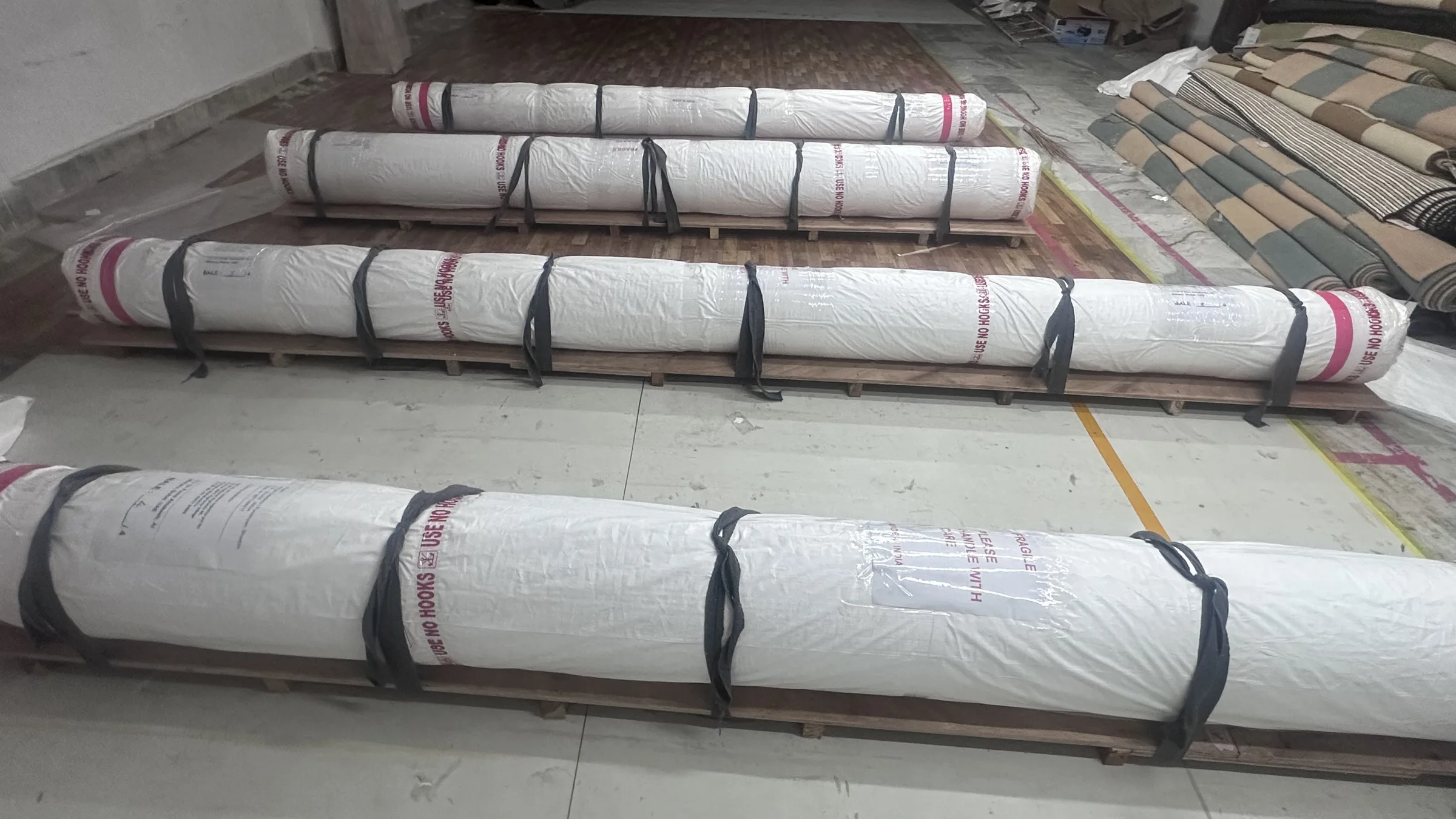 Four packed rugs strapped to wooden pallets with USE NO HOOKS and HANDLE WITH CARE printed on the wrap