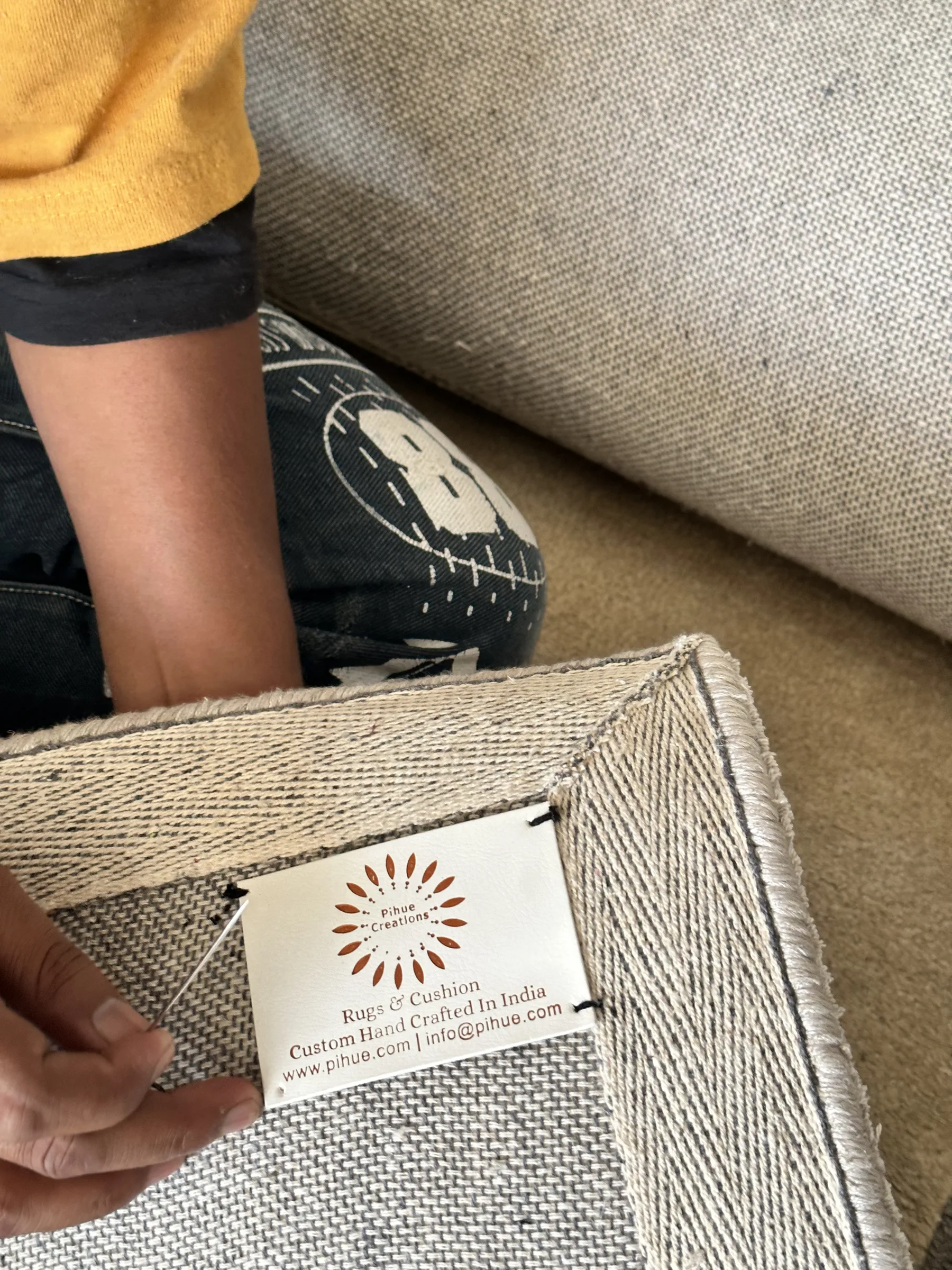 A PiHue Creations woven label being hand-sewn onto the reverse of a natural jute-and-cotton flatweave