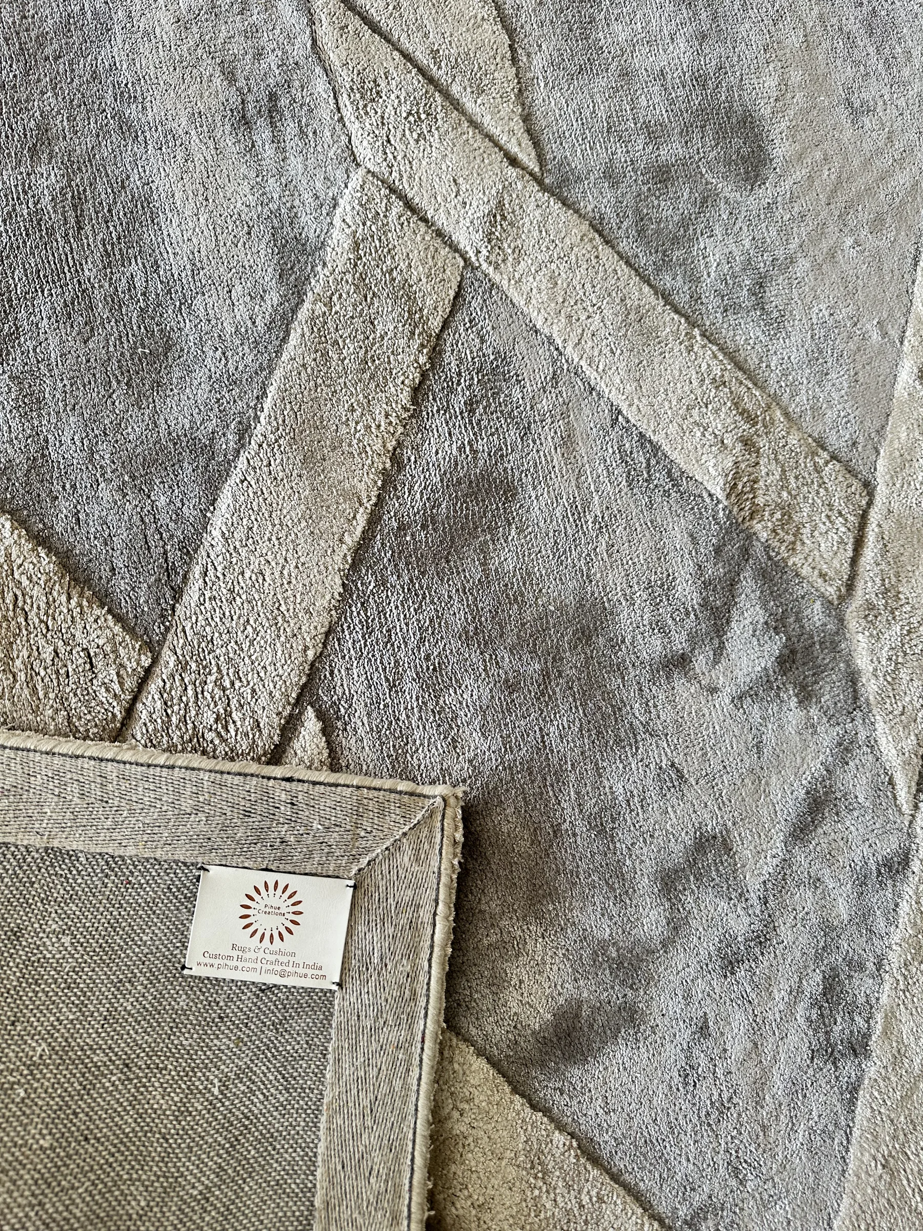 A PiHue Creations label sewn onto the reverse of a silver-grey silk-viscose rug with the corner folded up
