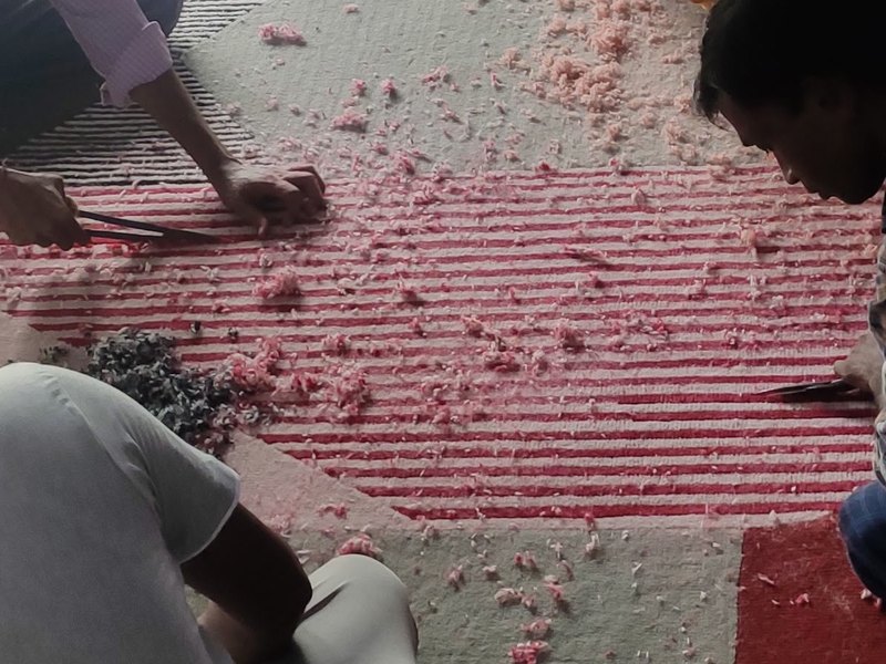 Close detail of hand-carving on a tufted rug, blade cutting ribbed relief into the pile