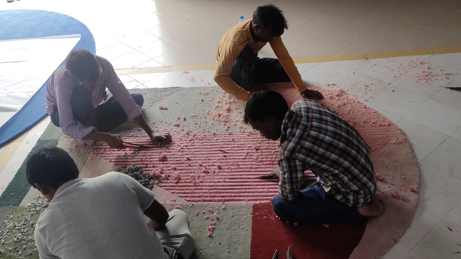 Four artisans hand-carving a large round tufted rug in Bhadohi, wool clippings across the surface