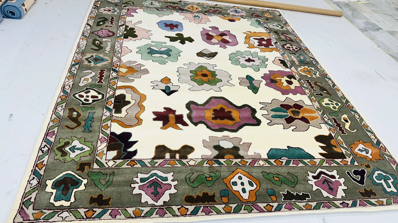 A finished hand-tufted rug with a colourful figurative floral border in pink, green, ochre and blue on cream ground