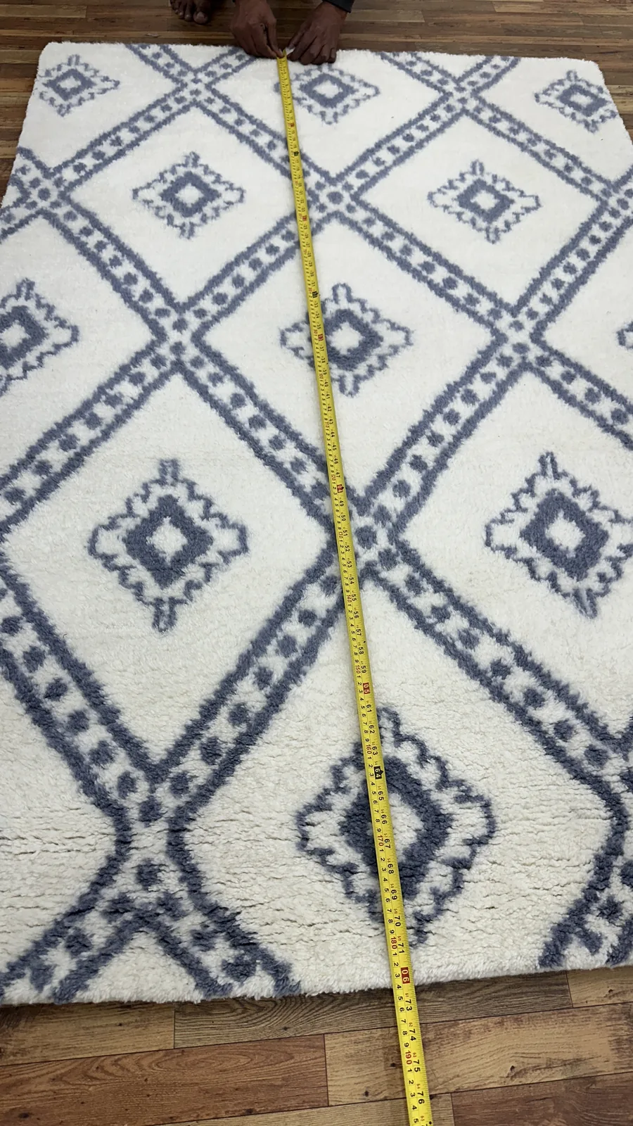 A hand-tufted rug on the floor with a yellow tape measure stretched down its full length, checked against the specified size