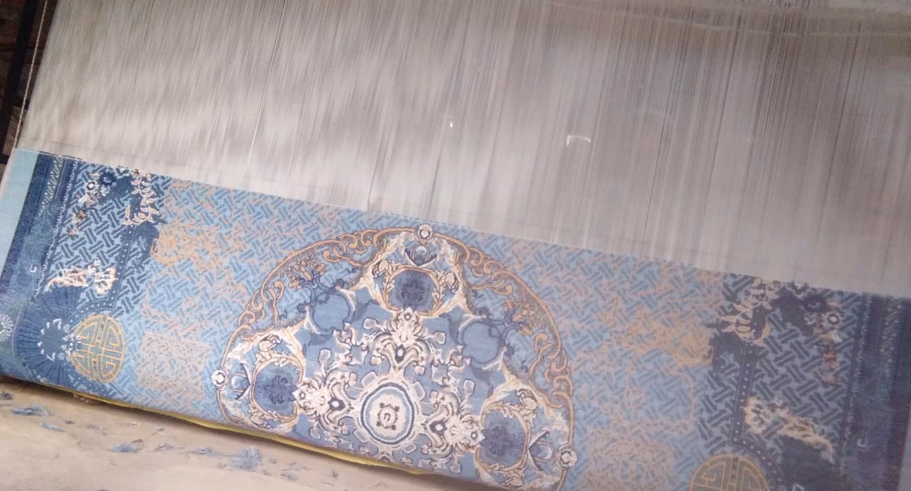 A blue silk rug in progress on the loom, the warp above and the woven face below