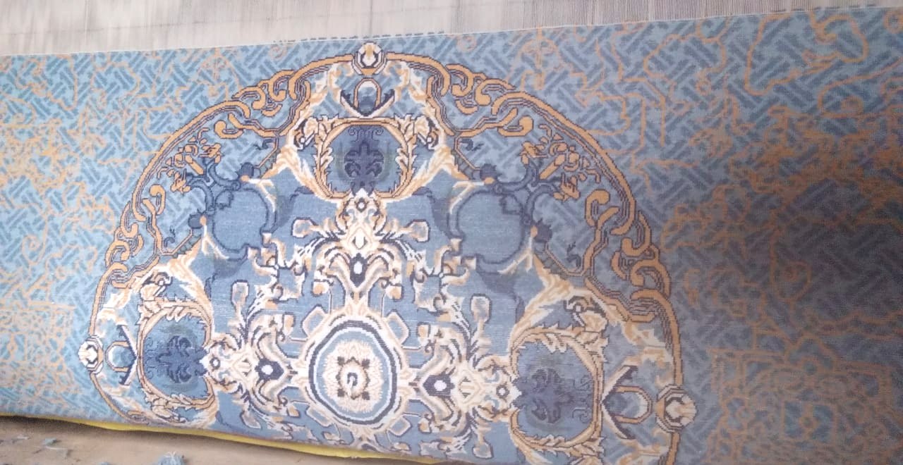 The medallion at the centre of the blue silk rug, mid-weave, individual knots visible
