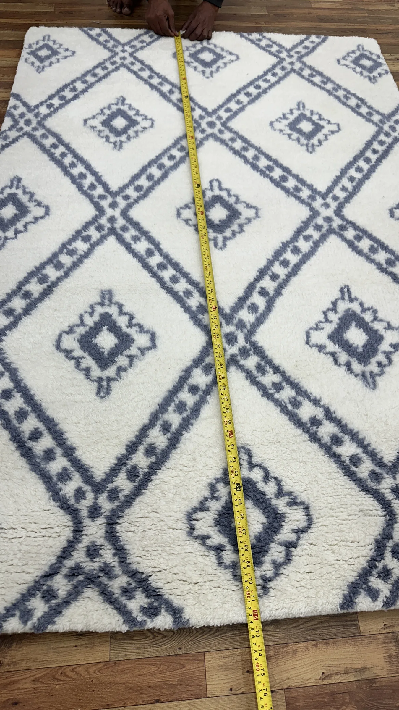 A finished rug's length being measured with a tape across the QC bench