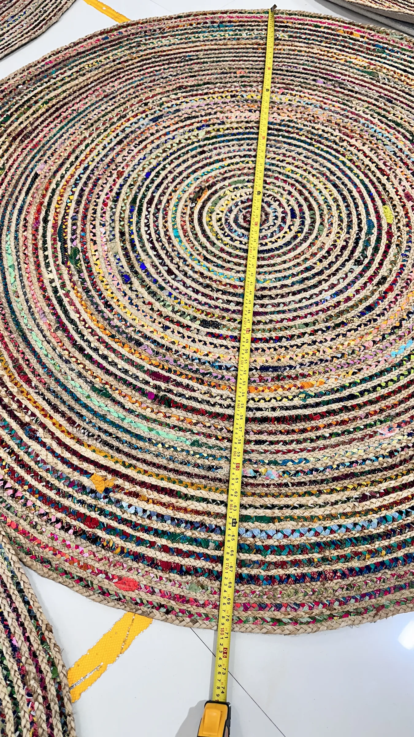 A large round braided rug being measured across the diameter with a yellow tape measure