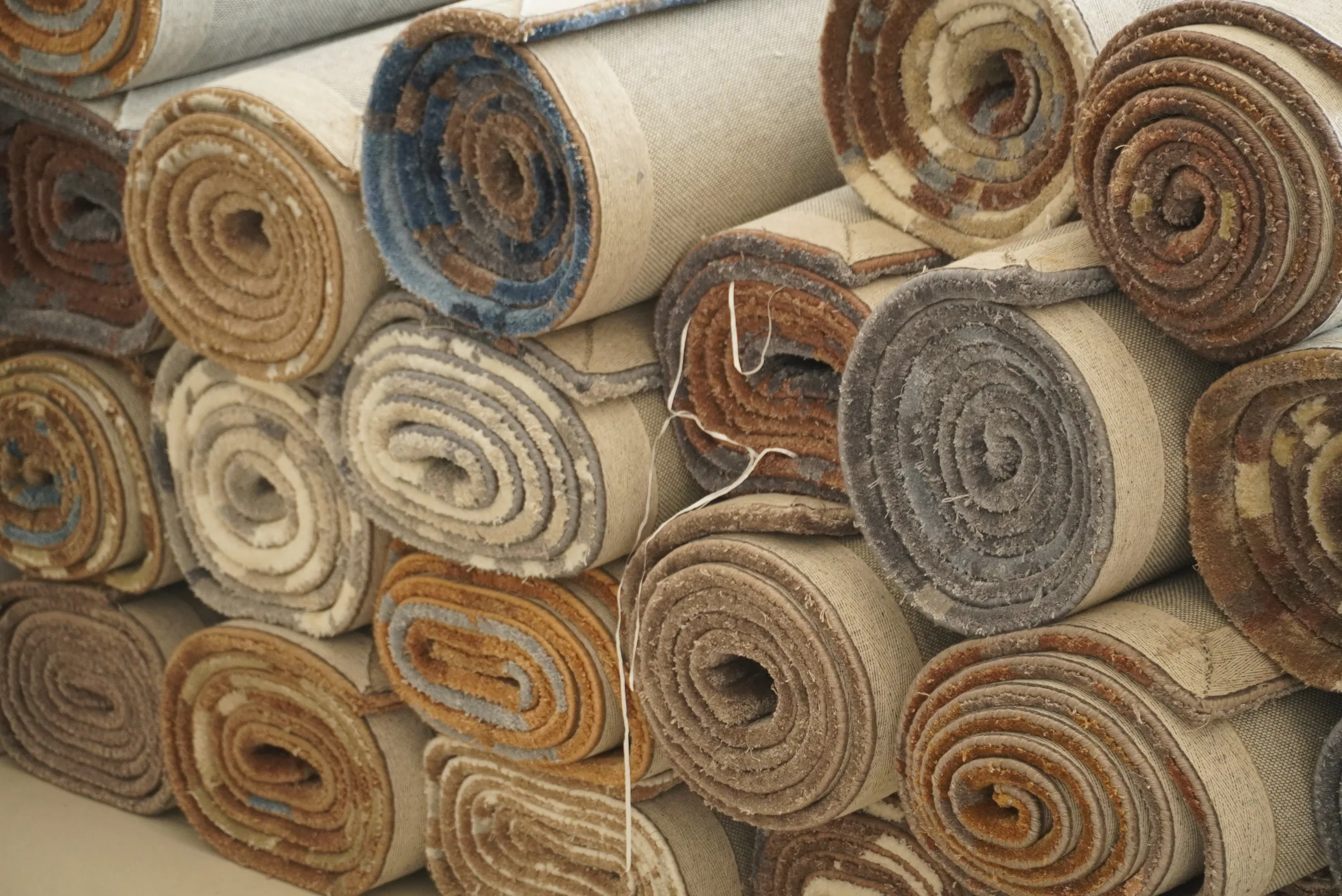 A stack of tightly rolled finished rugs in muted earth tones, cross-section visible