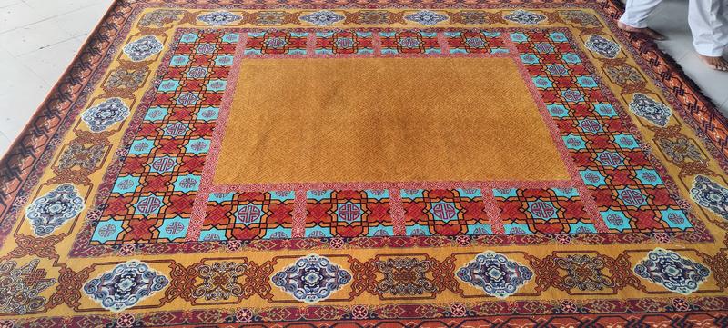 Hand-knotted rug with a plain gold field framed by turquoise, red and blue patterned borders