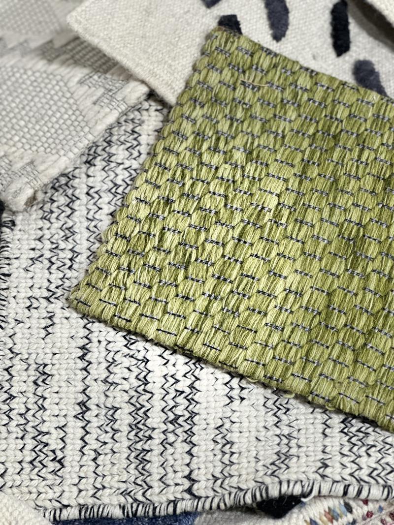 Olive textured weave swatch resting on ivory and navy zigzag flatweaves